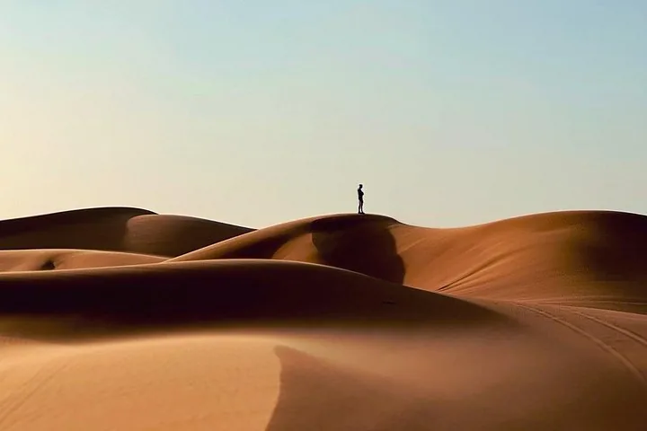 A tiny silhouette of a person standing atop a vast sand dune