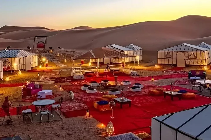 A luxury desert camp with white tents and red carpets at dusk