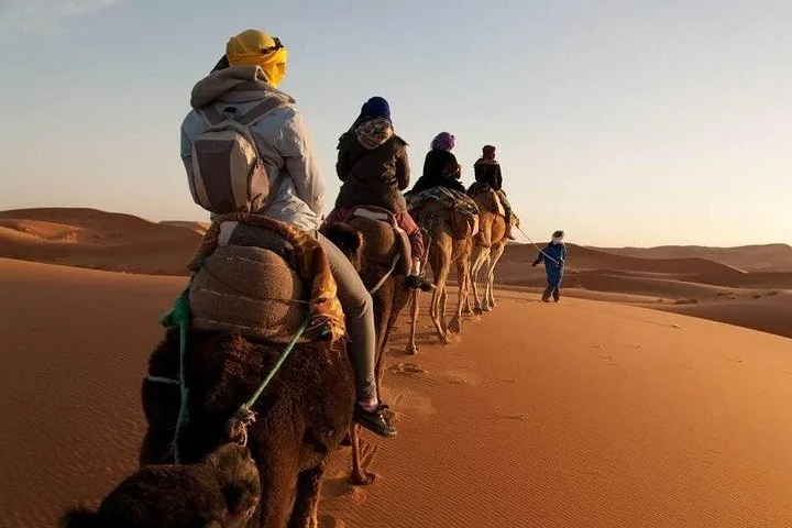 Tourists ride a camel caravan across the Erg Chebbi desert dunes
