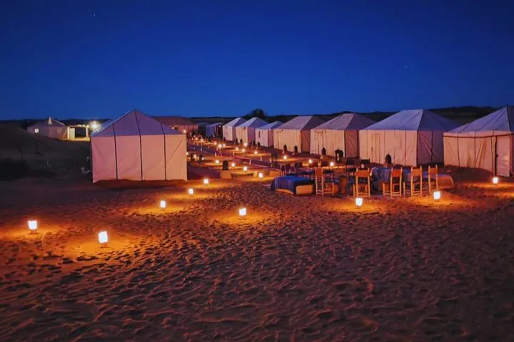 A desert camp illuminated by lanterns at night under a starry sky